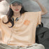 Person wearing a beige t-shirt with text, sitting against a concrete wall.